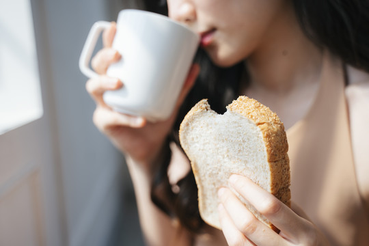 早上喝热咖啡时，女人手里咬着面包的剪影。