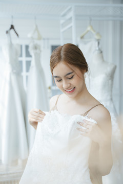 一位女士来到婚纱摄影棚试穿婚纱，她在镜子前举起白色的婚纱穿在身上。