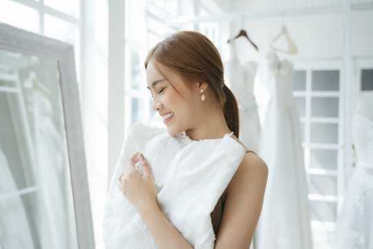一位女士来到婚纱摄影棚试穿婚纱，她在镜子前举起白色的婚纱穿在身上。