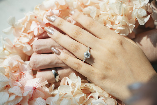 剪下的图像，男人和女人的手放在美丽的花朵上，戒指放在结婚戒指的手指上。