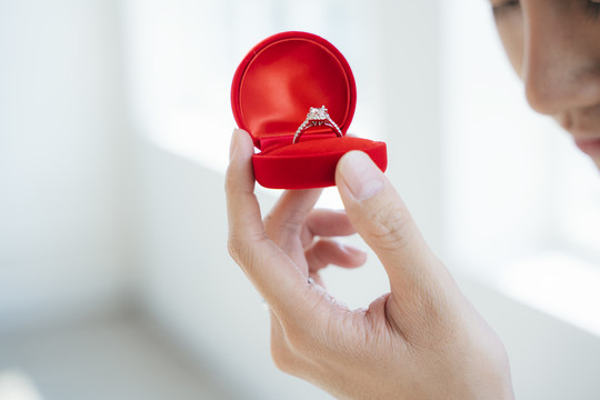 一个男人手里红色盒子里的结婚戒指的剪影。