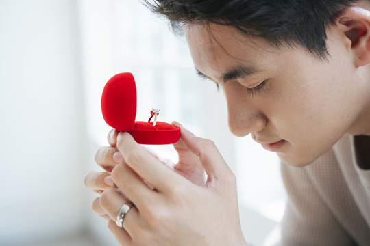 一个男人拿着红盒子里的结婚戒指准备向他的女朋友求婚的特写镜头。