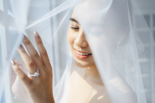 马尾金发女人在婚礼当天的早晨打扮好，站在窗前，用白色面纱遮住自己，摸了摸窗户，露出她的结婚戒指。