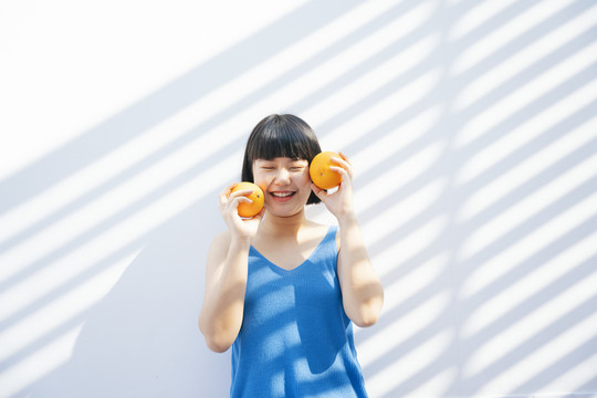 开朗美丽的鲍勃发型亚洲女人在蓝色背心衬衫举行两个橙色的热带水果白色背景。