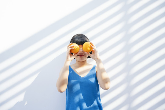 美丽搞笑的鲍勃发型穿着蓝色背心衬衫的亚洲女人拿着两个橘子假装戴着眼镜。
