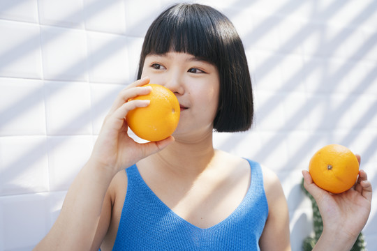 特写健康美丽的鲍勃发型穿着蓝色背心衬衫的亚洲女人喜欢吃热带橙色水果。
