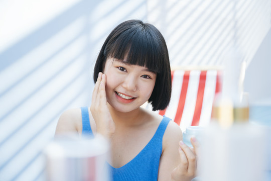 美丽的bob发型，穿着蓝色背心衬衫的亚洲女人，用化妆品罐涂抹乳霜。美容产品概念。紫外线防护。