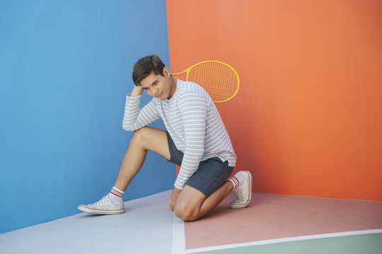 身着休闲服装、手持网球拍、背景为蓝橙色的迷人亚洲年轻男子。搞笑的姿势。打网球。拍拍姿势很酷。