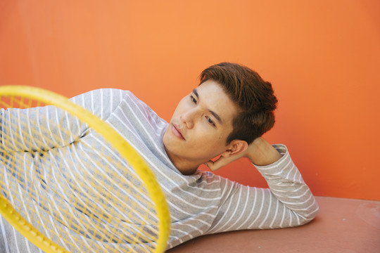 年轻英俊的亚洲男子网球运动员躺在橙色的地板上。