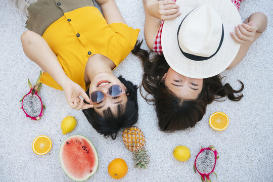 两个亚洲朋友躺在地上吃着热带水果。健康水果。顶视图。暑假。