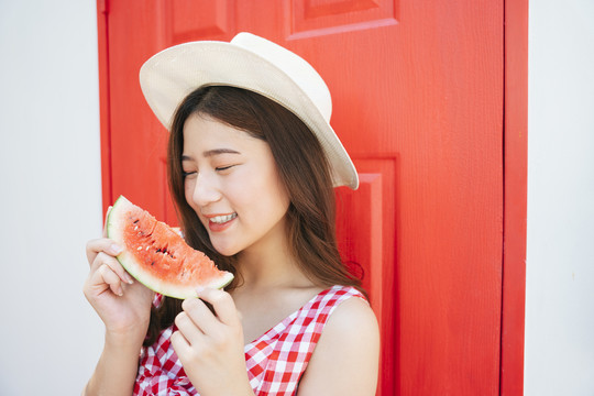 美丽的亚洲年轻女子在暑假拿着一片甜西瓜在红门上。