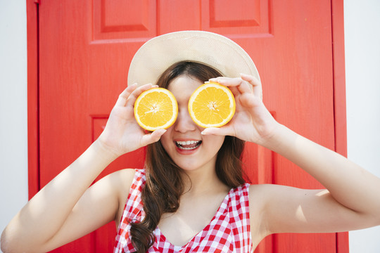 有趣美丽的亚洲年轻女子用一片橘子做眼镜。
