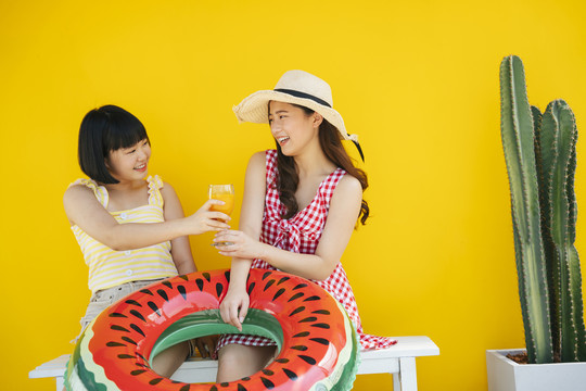 两个亚洲女人在暑假交了好朋友。一起在沙滩上旅行。在黄色背景上。