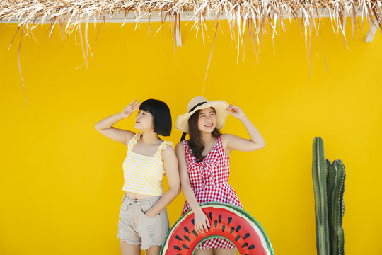 两个亚洲女人在暑假交了好朋友。一起在沙滩上旅行。在黄色背景上。