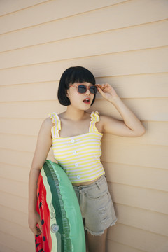 鲍勃理发美丽的亚洲年轻女子穿着黄色背心和太阳镜与救生圈或游泳筒合影。