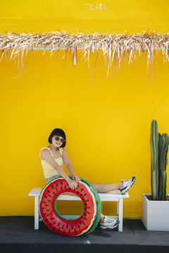 可爱漂亮的亚洲年轻女子，身穿黄色背心，戴着墨镜，橙色背景下有游泳筒。在海滩度暑假。