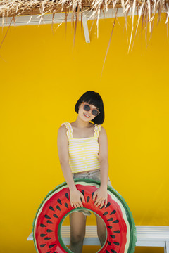 可爱漂亮的亚洲年轻女子，身穿黄色背心，戴着墨镜，橙色背景下有游泳筒。在海滩度暑假。