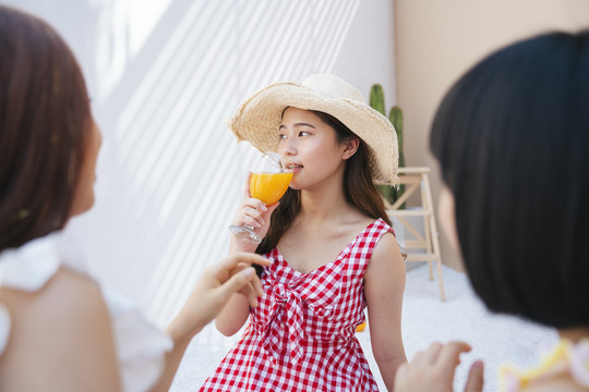 美丽的亚洲年轻女子戴着帽子，穿着红裙子，和朋友在夏日派对上喝着橙汁。