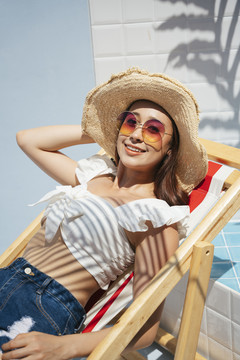 美丽的亚洲年轻女子戴着草帽和太阳镜躺在沙滩椅上。暑假。