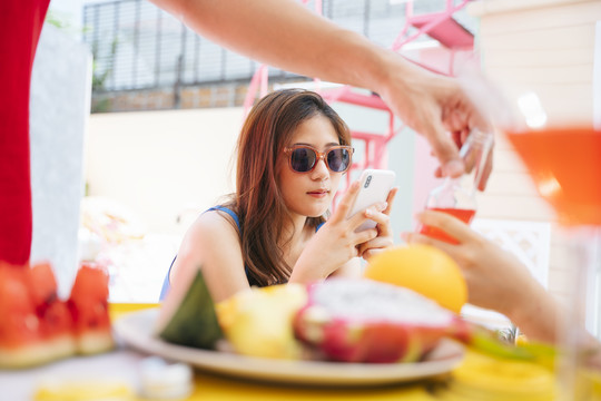 美丽的亚洲女人戴着太阳镜坐在热带岛屿的酒吧里向酒保点果汁。