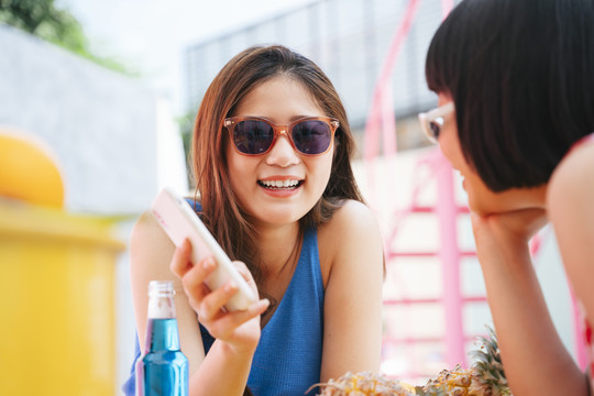 一位戴着眼镜的美丽亚洲年轻女子在酒吧里和人们谈论社交媒体上发生的事情。手机用户。问外国人。