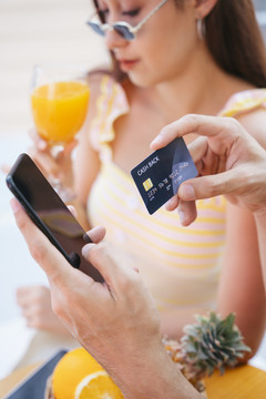 暑假度假时用智能手机和信用卡支付酒店预订费用的男子。