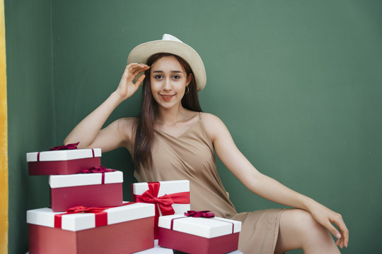 性感的亚洲年轻女子戴着帽子坐在礼物盒隔离在绿色背景。