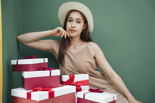 性感的亚洲年轻女子戴着帽子坐在礼物盒隔离在绿色背景。