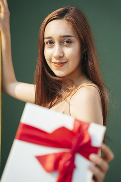 在绿色背景上，手持红丝带礼盒的美丽黑发女子的特写肖像。