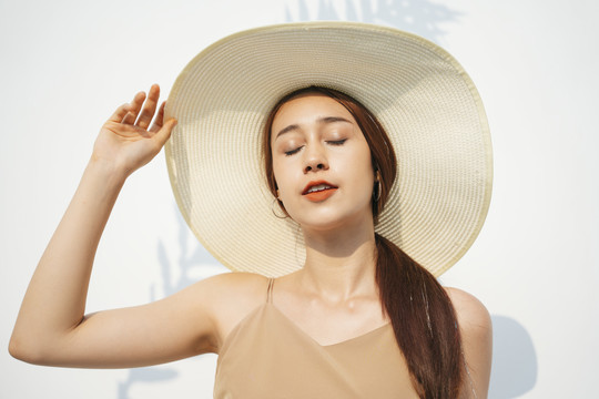 白色背景上戴着大帽子的漂亮黑发女人的特写镜头。暑假。商业用途。化妆品概念。