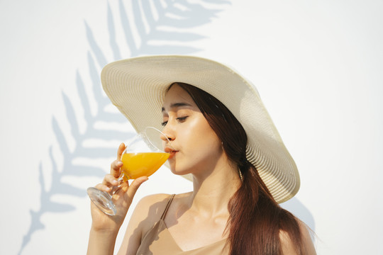 美丽迷人的黑发女子戴着帽子喝着橙汁从玻璃杯隔离在白色背景。天然橙汁。