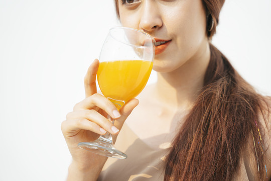 在白色背景下，一个漂亮的黑发女人在玻璃杯中喝橙汁。