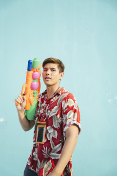 英俊的泰国当地男子身穿彩色花布手持水枪。隔离在柔和的蓝色背景上。泰国的泼水节。