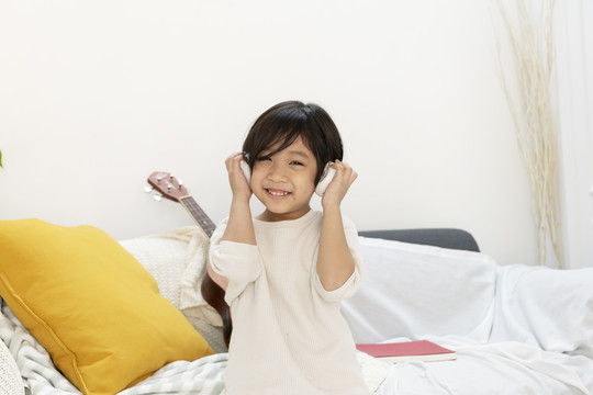 快乐有趣的亚洲小男孩喜欢坐在客厅的沙发上用无线耳机听音乐。