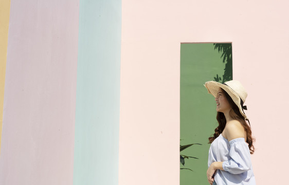 年轻的泰国亚裔妇女在暑假戴草帽。在度假村散步。粉彩墙。