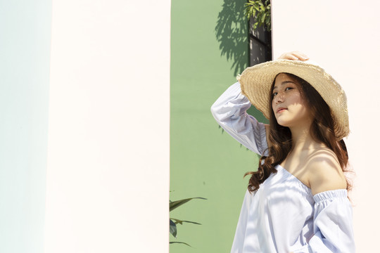 美丽的亚洲女人，戴着草帽在暑假旅行。背景是粉红色的墙。