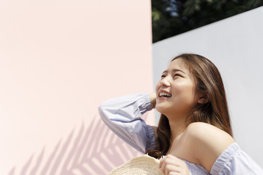 美丽的亚洲女人，戴着草帽在暑假旅行。背景是粉红色的墙。