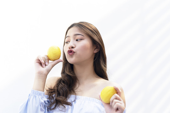 快乐美丽的亚洲年轻女子拿着两个柠檬隔着白色的背景。