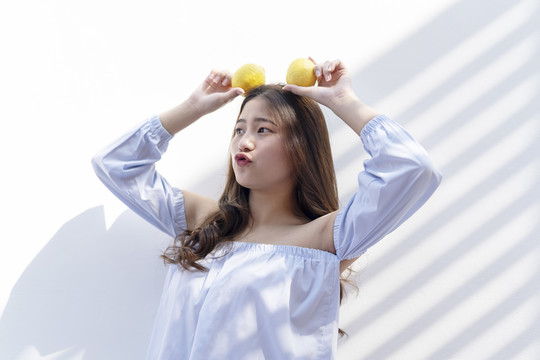 快乐美丽的亚洲年轻女子，手拿两个橘子，在白色背景上分开。