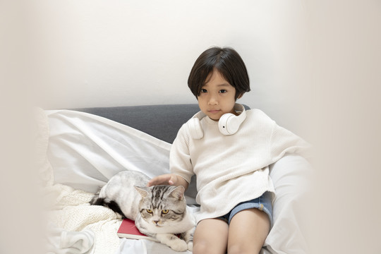 穿着白衬衫的可爱小男孩在客厅的沙发上和毛茸茸的猫玩耍。