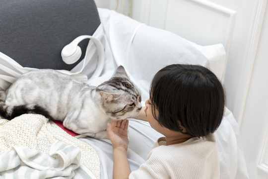 一个亚洲小男孩试图亲吻躺在客厅沙发上的猫。