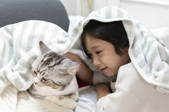 亚洲可爱的小男孩在毯子下面玩猫。