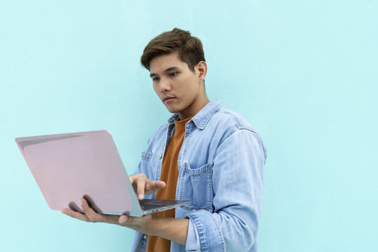 年轻英俊的亚泰男子穿着休闲夹克，手拿笔记本电脑。在绿薄荷色背景上隔离。