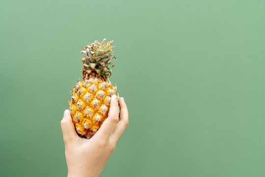 一个女人手拿菠萝隔离在绿色背景。热带水果的复制空间。