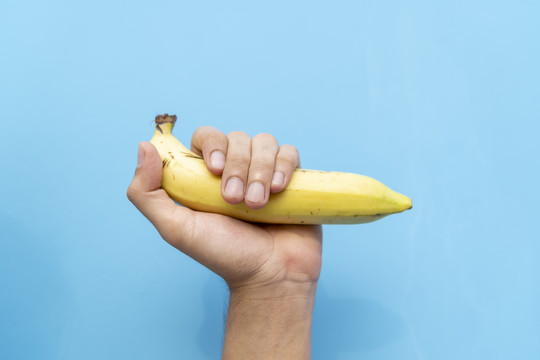 一只手拿着新鲜成熟的香蕉隔离在蓝色背景上。健康水果产品。