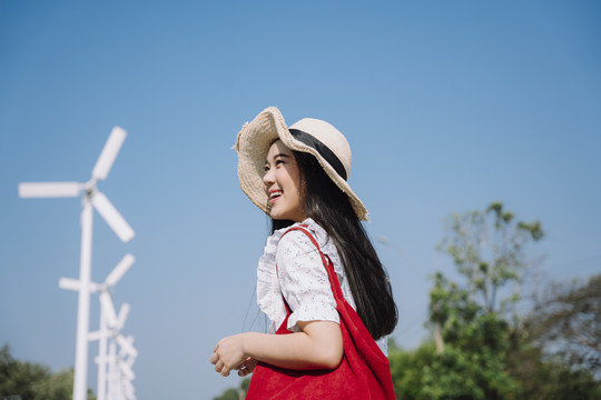 长发女人，穿着长裙，戴着帽子，带着风车走在风和日丽的蓝天上。