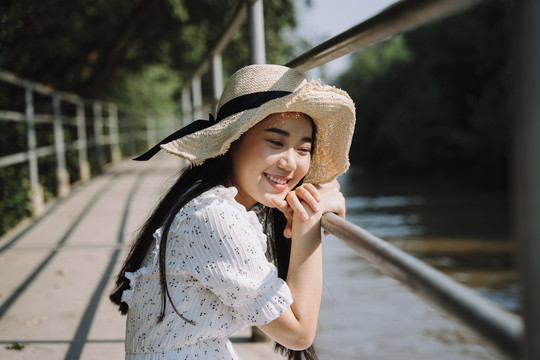 阳光明媚的日子里，一个戴着帽子的长发女人坐在红树林旁的小码头上，抓住码头的扶手。