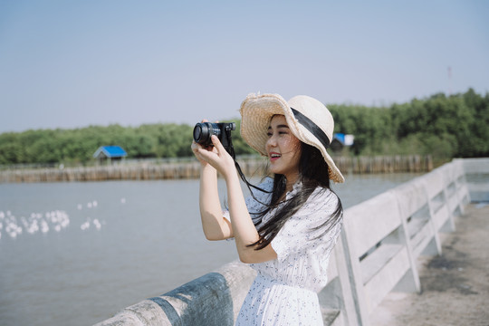 风和日丽，戴着帽子和连衣裙的长发女人用黑色照相机拍摄大海。