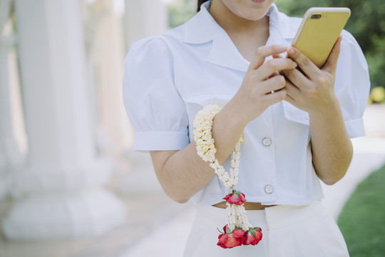 这名妇女走到庙里用智能手机时手腕上戴着茉莉花环的剪影。