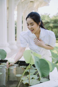 身穿白衬衫的黑马尾女子弯腰抓住庙里盆里的白莲花。